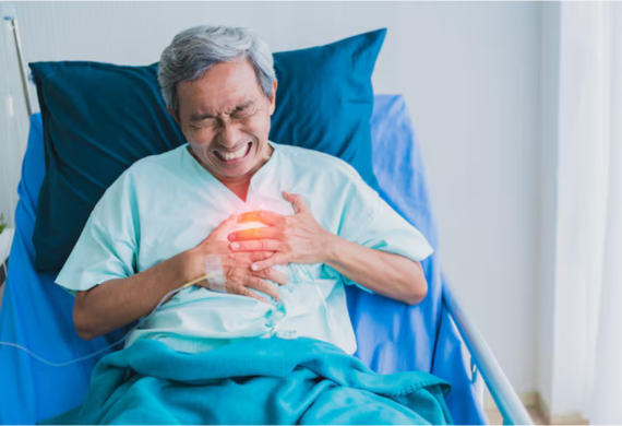 A man seated on the hospital bed clutching his chest in pain.
