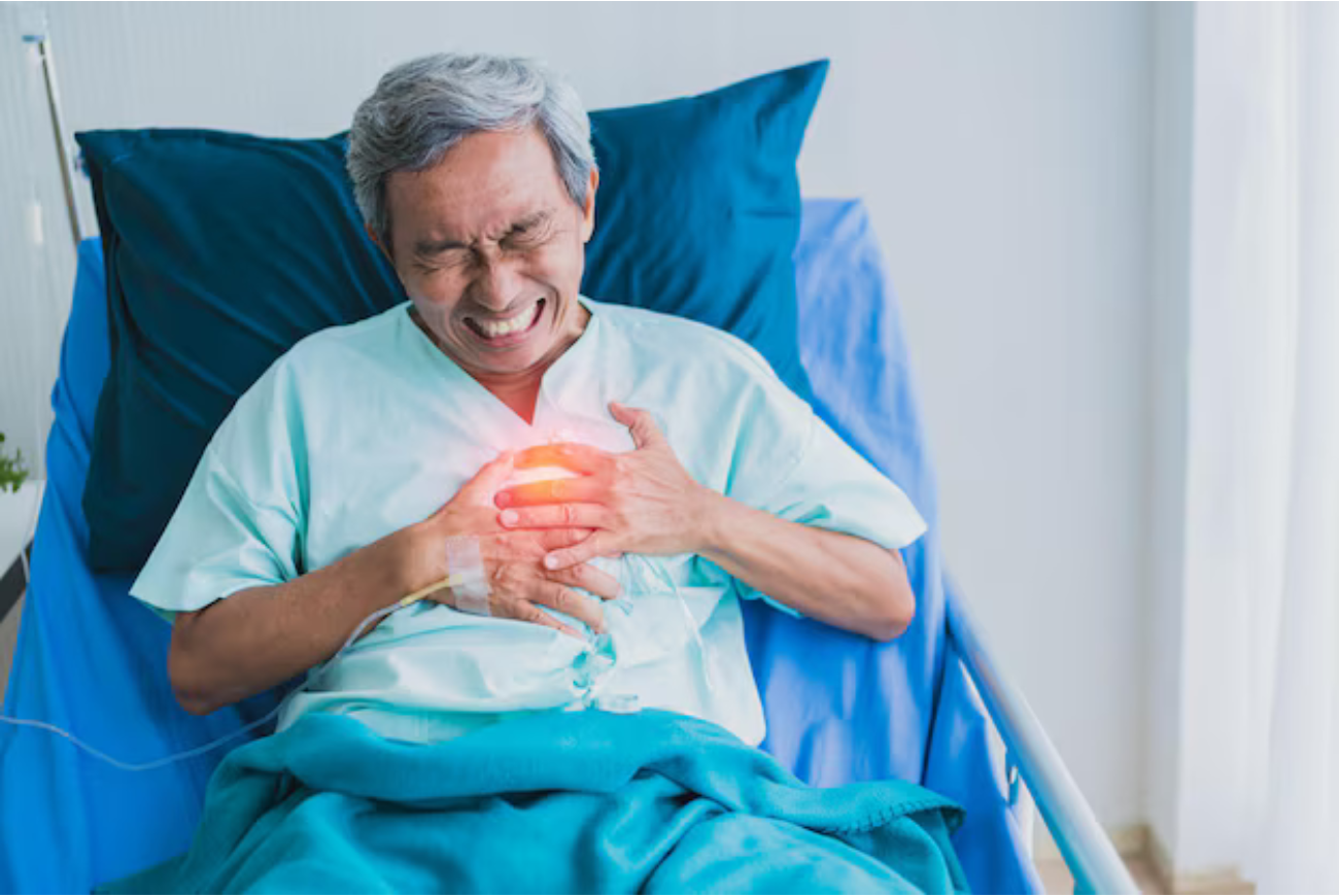 A man seated on the hospital bed clutching his chest in pain.