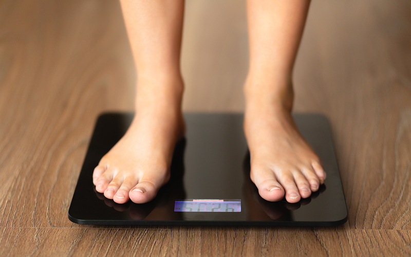 Person standing on scale monitoring weight for heart health.