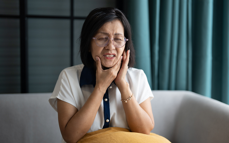 Senior woman holding her jaw in pain from facial numbness.