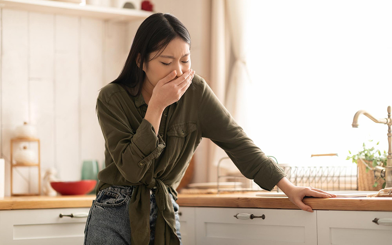Nauseous woman covering her mouth, a subtle heart attack sign.