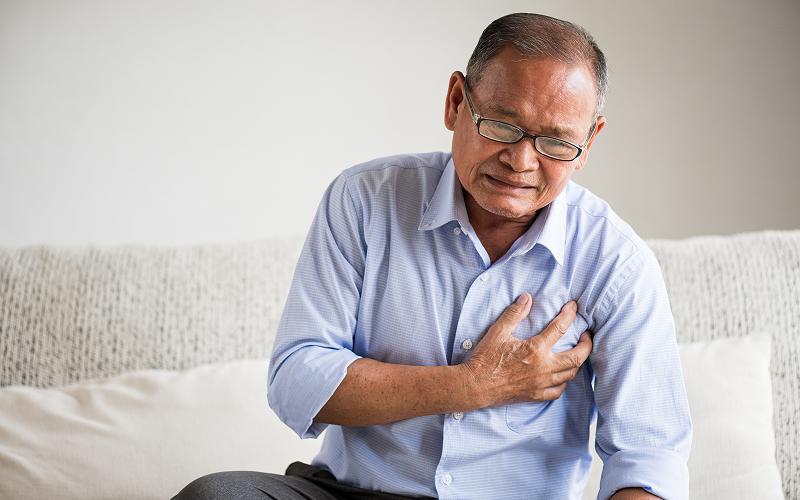 Elderly man clutching chest experiencing symptoms of heart disease